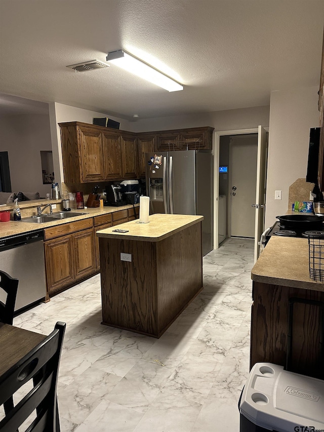 kitchen with visible vents, a kitchen island, appliances with stainless steel finishes, marble finish floor, and a sink