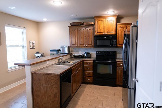 kitchen featuring dark countertops, decorative backsplash, a sink, a peninsula, and black appliances