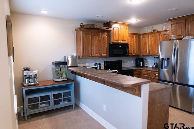 kitchen featuring a peninsula, brown cabinets, black appliances, tasteful backsplash, and dark countertops