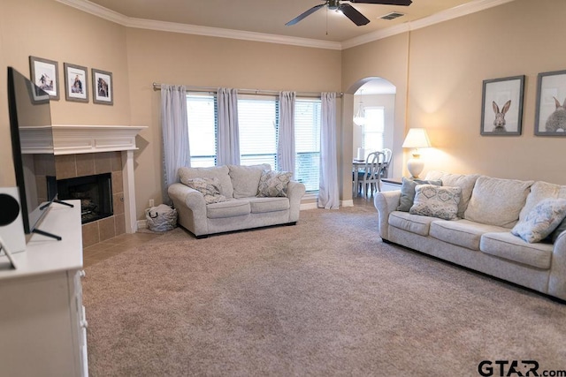 carpeted living area featuring arched walkways, crown molding, a fireplace, visible vents, and a ceiling fan