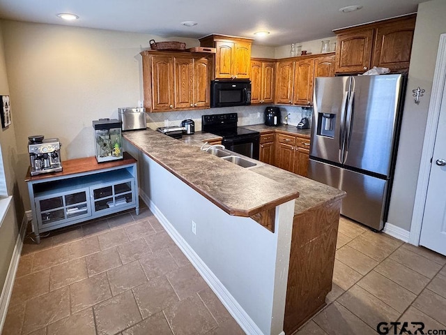 kitchen with a peninsula, a sink, baseboards, black appliances, and brown cabinetry