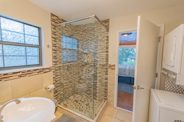 bathroom with stacked washer and clothes dryer, tile walls, tile patterned flooring, and a shower with door