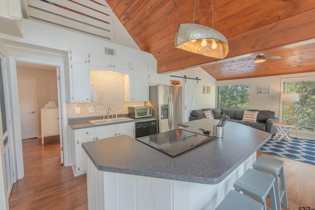 kitchen featuring lofted ceiling, a barn door, sink, white cabinetry, and appliances with stainless steel finishes