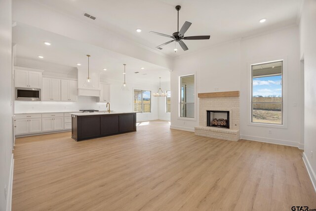 kitchen with decorative light fixtures, a brick fireplace, stainless steel appliances, a kitchen island with sink, and white cabinets