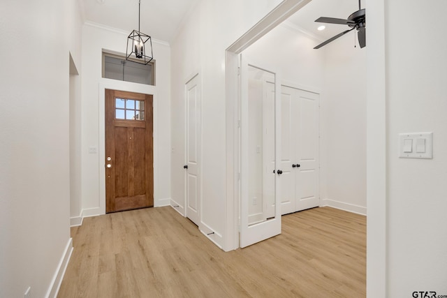 entrance foyer with ceiling fan with notable chandelier, ornamental molding, a towering ceiling, and light wood-type flooring