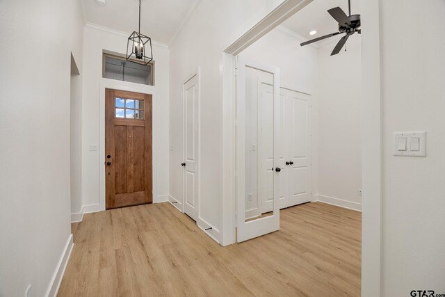 entryway with ornamental molding, a towering ceiling, ceiling fan with notable chandelier, and light wood-type flooring