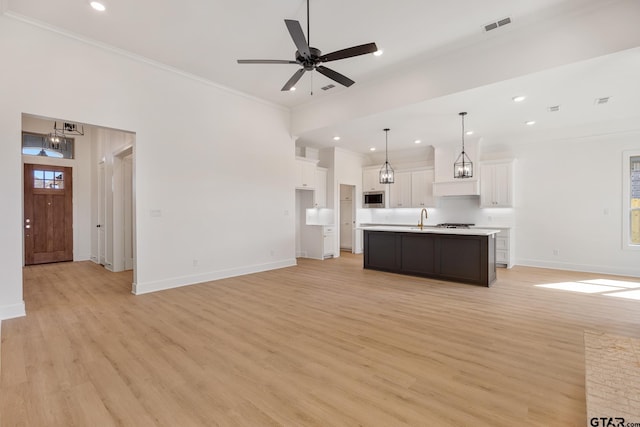 kitchen featuring decorative light fixtures, light hardwood / wood-style floors, white cabinets, and a kitchen island with sink