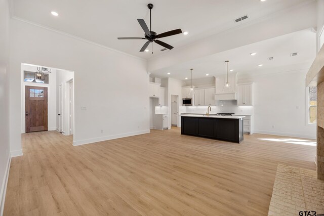 kitchen featuring pendant lighting, stainless steel microwave, a kitchen island with sink, and white cabinets