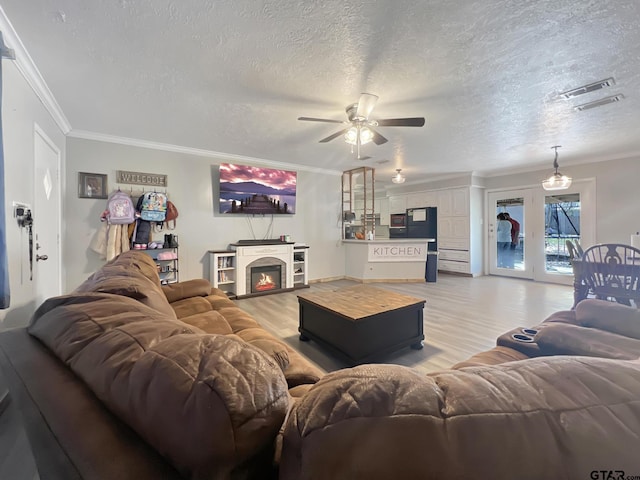 living room featuring ceiling fan, crown molding, light hardwood / wood-style flooring, and a textured ceiling