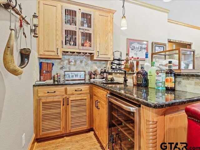 bar with dark stone counters, backsplash, hanging light fixtures, beverage cooler, and light hardwood / wood-style flooring