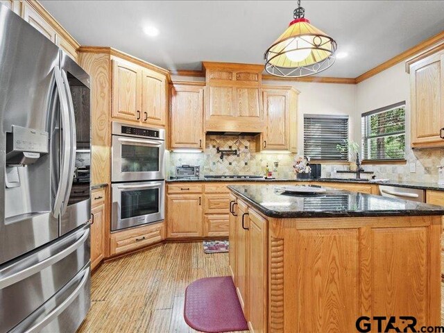 kitchen featuring crown molding, appliances with stainless steel finishes, pendant lighting, light hardwood / wood-style floors, and dark stone countertops