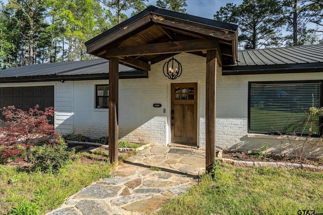 entrance to property with brick siding, a garage, and metal roof