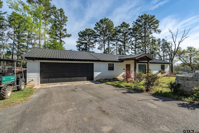 ranch-style home with driveway, metal roof, and a garage