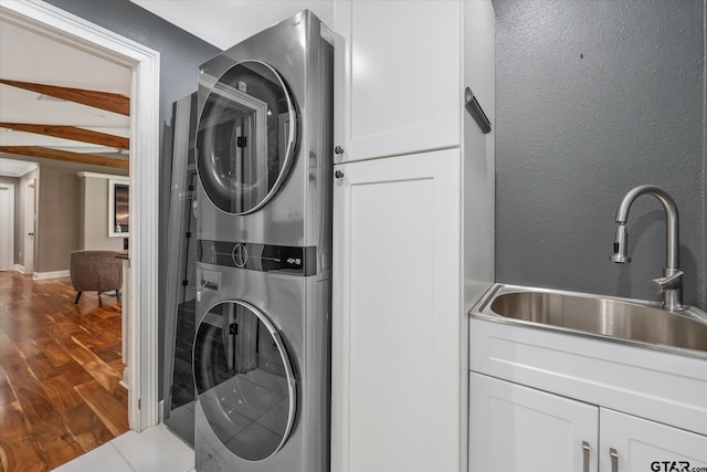 laundry area with stacked washer / drying machine, wood finished floors, a sink, and cabinet space