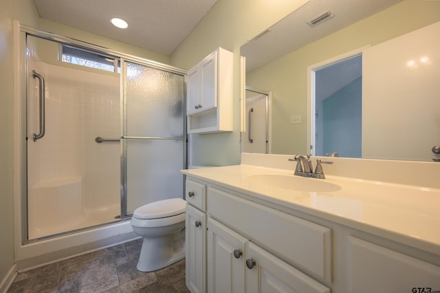 bathroom featuring vanity, toilet, a shower with shower door, and a textured ceiling