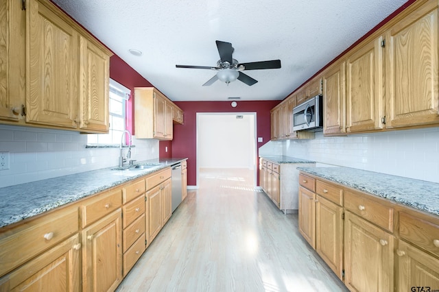 kitchen featuring sink, light stone counters, ceiling fan, stainless steel appliances, and light hardwood / wood-style floors