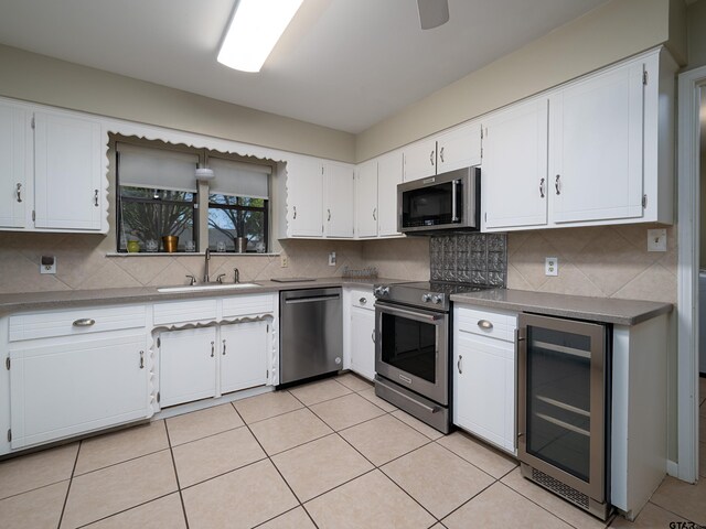 kitchen with tasteful backsplash, white cabinets, appliances with stainless steel finishes, a sink, and beverage cooler