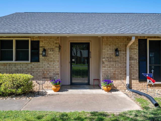 property entrance featuring brick siding and a shingled roof
