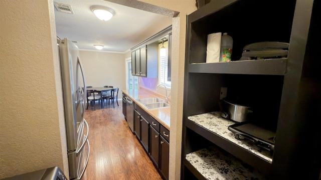 kitchen featuring sink, light hardwood / wood-style flooring, appliances with stainless steel finishes, ornamental molding, and light stone countertops