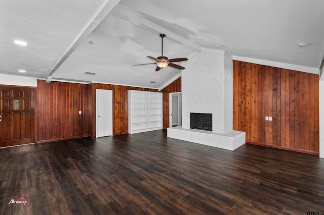 unfurnished living room featuring wood walls, dark hardwood / wood-style floors, ceiling fan, vaulted ceiling with beams, and a brick fireplace