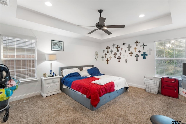 carpeted bedroom with ceiling fan and a raised ceiling