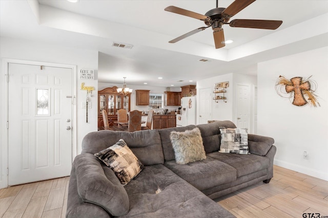 living room featuring ceiling fan with notable chandelier, light hardwood / wood-style flooring, and a raised ceiling