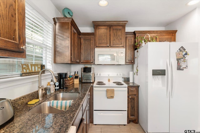 kitchen with dark stone countertops, white appliances, sink, and light tile patterned floors