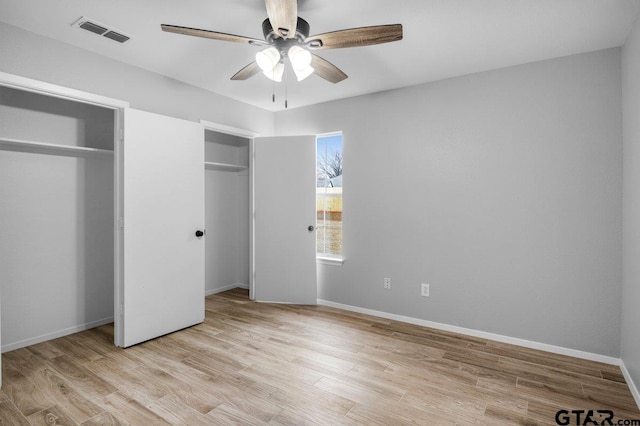 unfurnished bedroom featuring light wood-style floors, baseboards, visible vents, and two closets