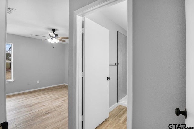 hall with light wood-style flooring, visible vents, and baseboards