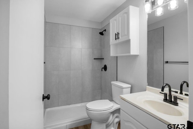 full bathroom with toilet, a tile shower, and vanity