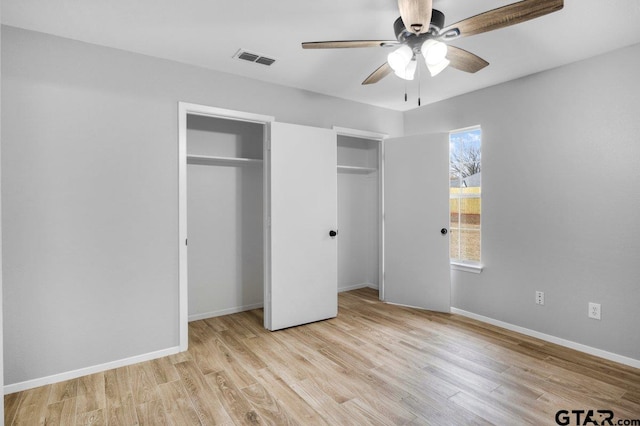 unfurnished bedroom featuring wood finished floors, a ceiling fan, visible vents, baseboards, and two closets