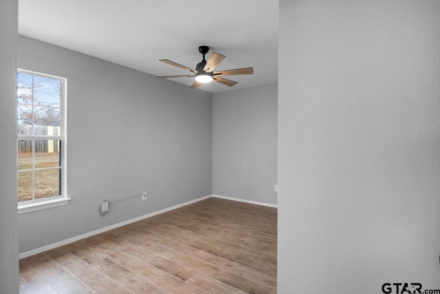 empty room featuring light wood finished floors, ceiling fan, baseboards, and a wealth of natural light