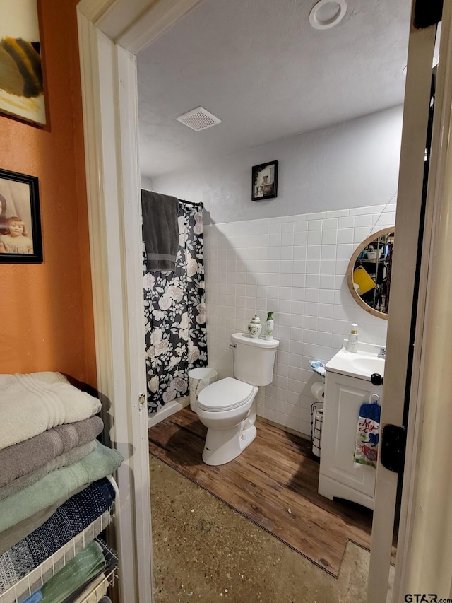 bathroom with tile walls, wood-type flooring, toilet, and vanity