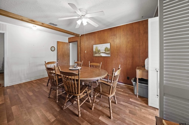 dining area with beam ceiling, ceiling fan, wooden walls, hardwood / wood-style flooring, and a textured ceiling