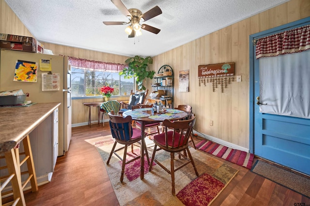 dining room with a textured ceiling, wood walls, ceiling fan, and wood-type flooring