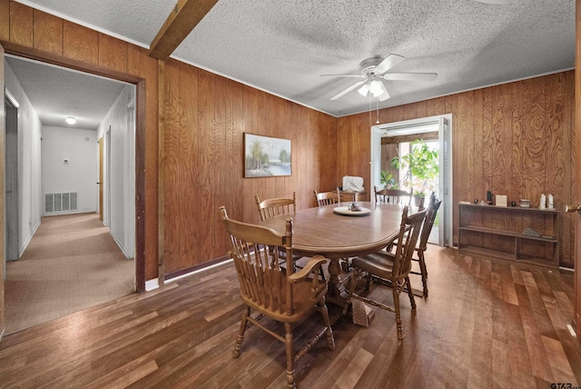 dining space featuring dark wood-type flooring, ceiling fan, beamed ceiling, and wooden walls