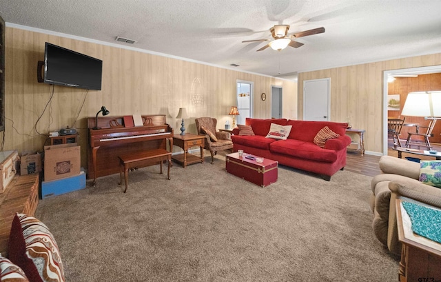 living room featuring a textured ceiling, carpet floors, ceiling fan, and crown molding