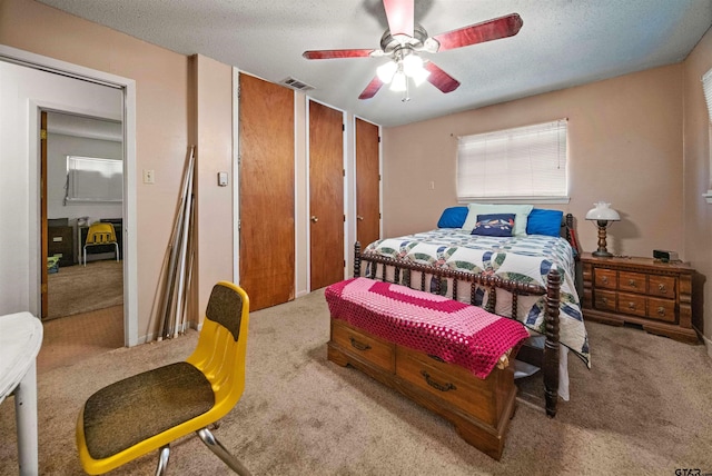 bedroom with ceiling fan, light colored carpet, multiple closets, and a textured ceiling