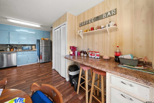 kitchen featuring wood walls, appliances with stainless steel finishes, blue cabinetry, dark hardwood / wood-style flooring, and a textured ceiling