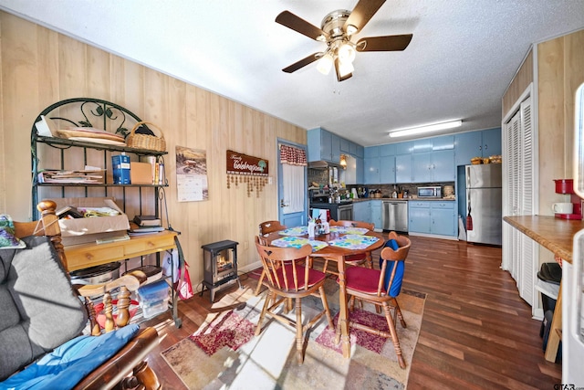 dining space featuring a textured ceiling, ceiling fan, wooden walls, and dark hardwood / wood-style floors