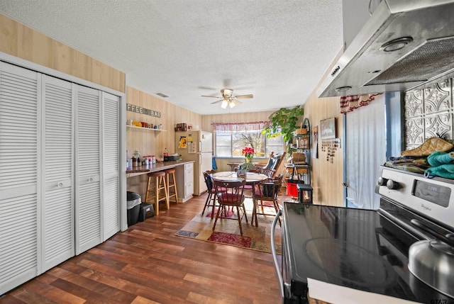 kitchen with a textured ceiling, wall chimney exhaust hood, white fridge, stainless steel electric stove, and ceiling fan