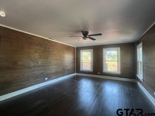 spare room with wooden walls, dark wood-style flooring, a ceiling fan, and baseboards