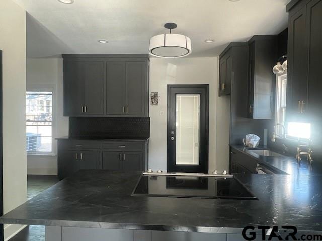 kitchen with black electric cooktop, a peninsula, a sink, dark countertops, and pendant lighting