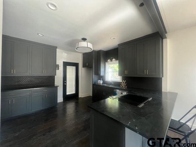 kitchen featuring a peninsula, tasteful backsplash, gray cabinets, and dark wood-style flooring