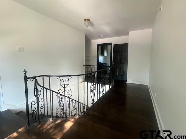 corridor with dark wood-style flooring, an upstairs landing, and baseboards