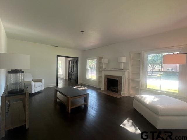 living room featuring baseboards, dark wood finished floors, built in features, and a healthy amount of sunlight