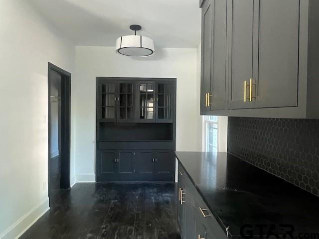 interior space with dark wood-style floors, dark countertops, gray cabinets, glass insert cabinets, and baseboards