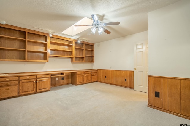 unfurnished office with built in desk, light carpet, ceiling fan, a textured ceiling, and wooden walls