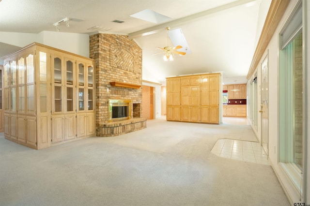 unfurnished living room with a fireplace, light colored carpet, ceiling fan, and vaulted ceiling with skylight