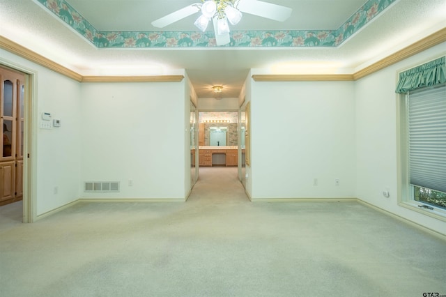 carpeted spare room with ceiling fan, crown molding, and a tray ceiling